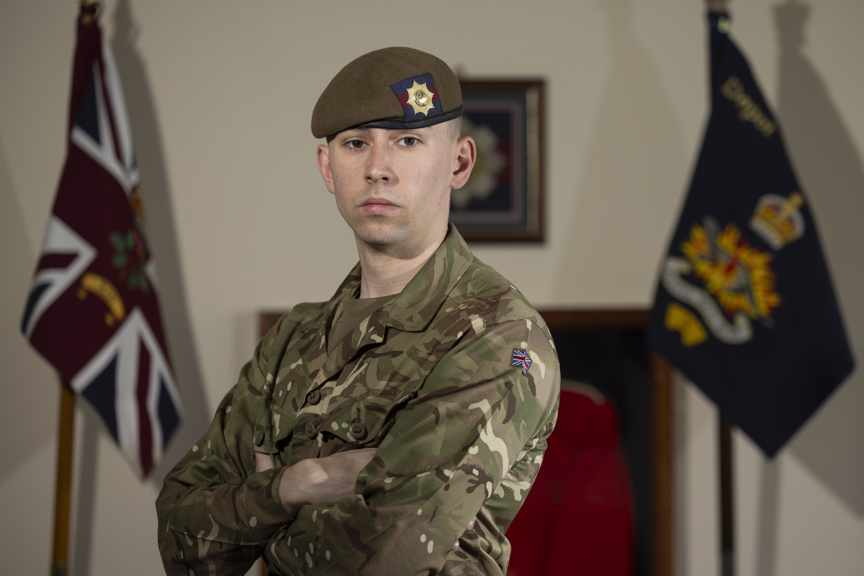 Guardsman stood posing in his camouflage uniform with beret on showing a coldstream guards cap badge.