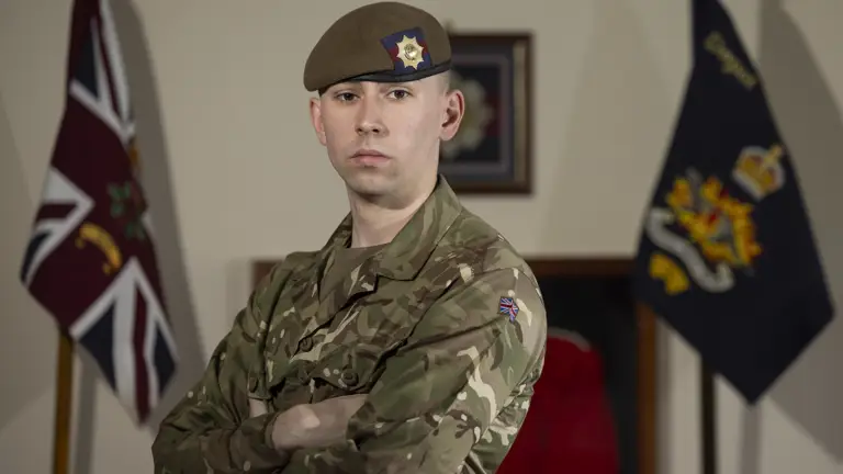 Guardsman stood posing in his camouflage uniform with beret on showing a coldstream guards cap badge.