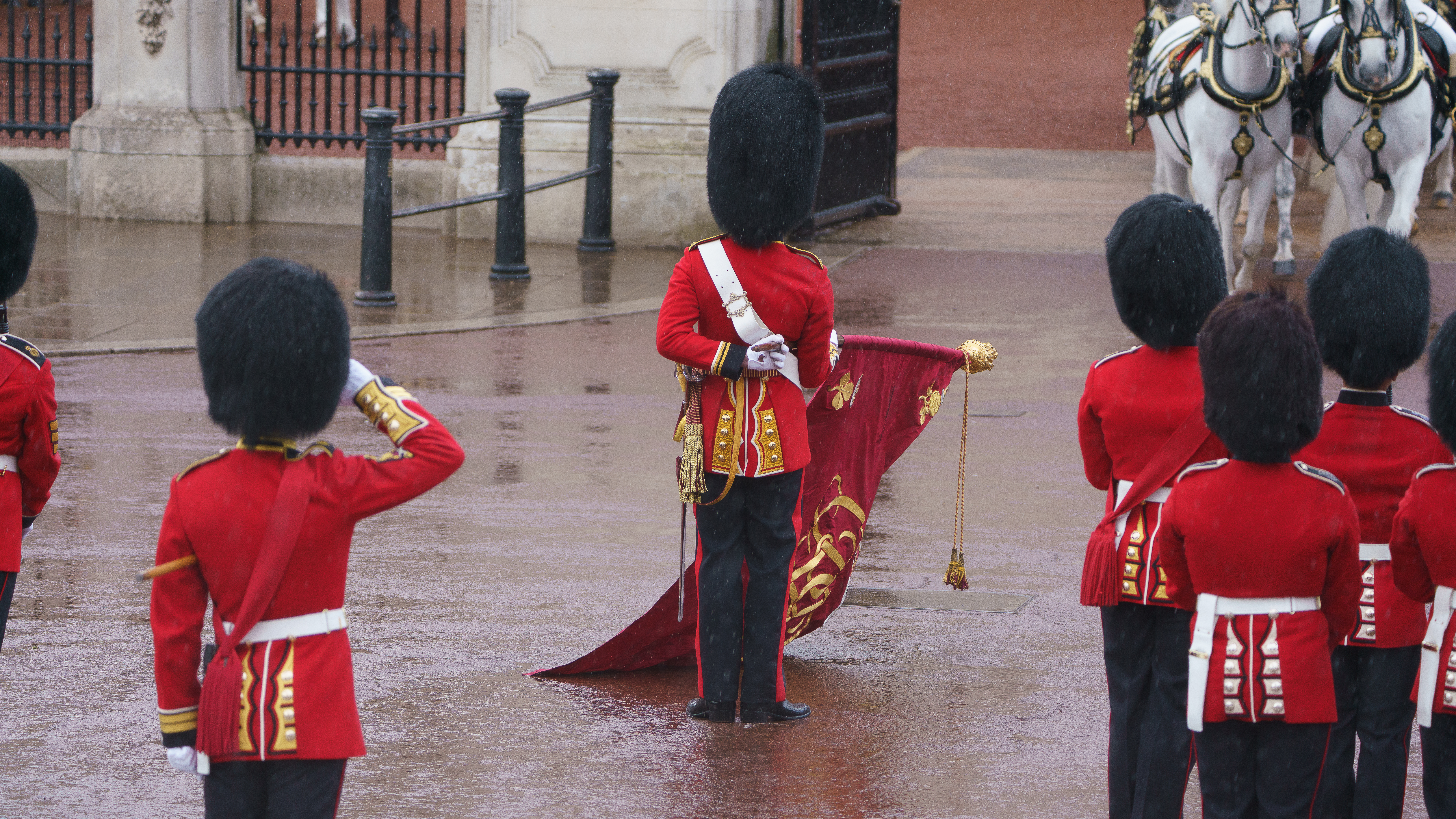 A group of guards in red uniforms and black bearskin hats perform a ceremonial duty in a courtyard. 
