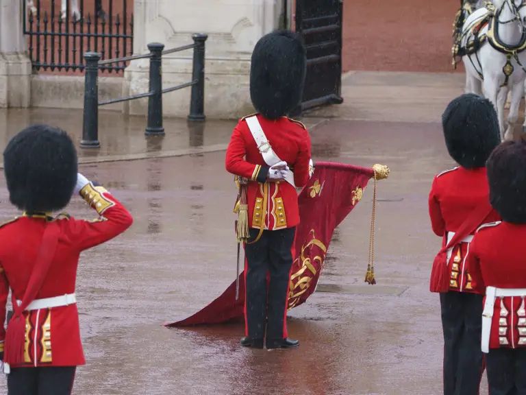 A group of guards in red uniforms and black bearskin hats perform a ceremonial duty in a courtyard.