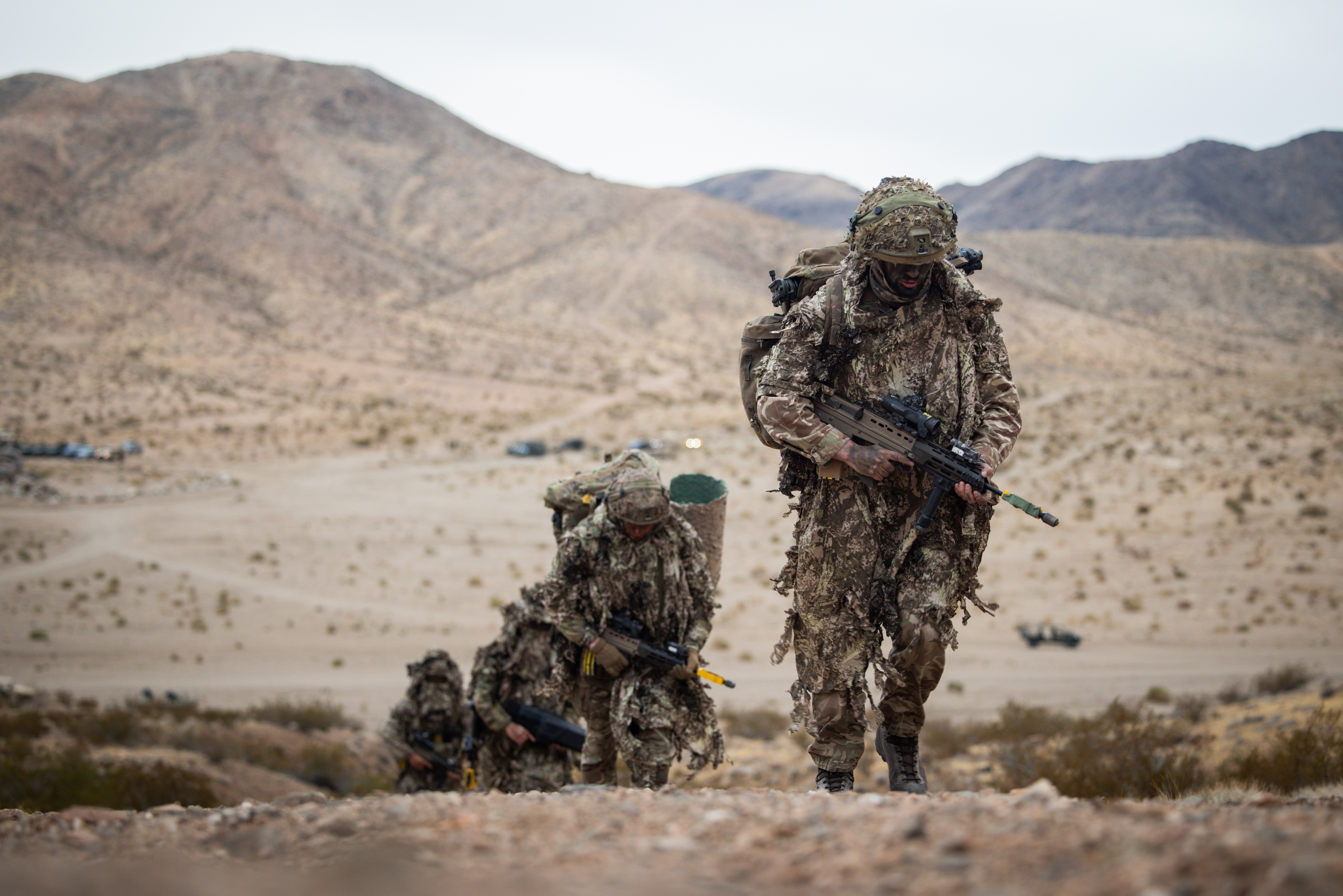 Soldiers wearing camouflage suits climb up a mountain carrying their equipment.