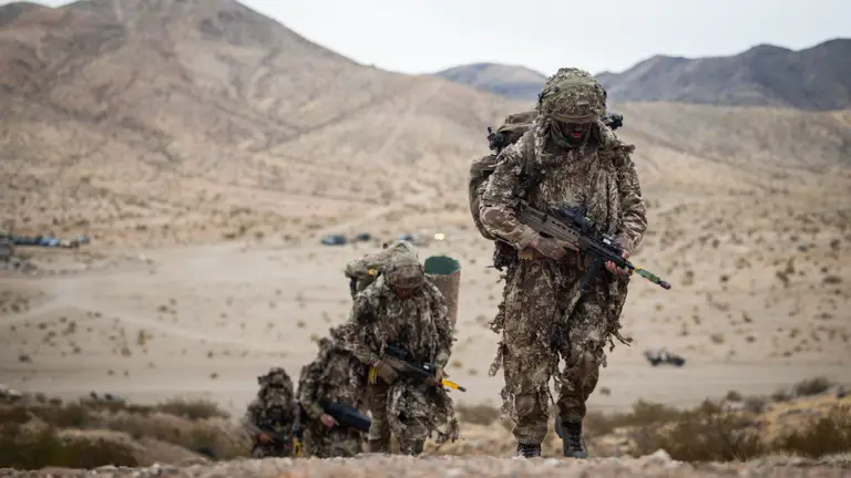 Soldiers wearing camouflage suits climb up a mountain carrying their equipment.