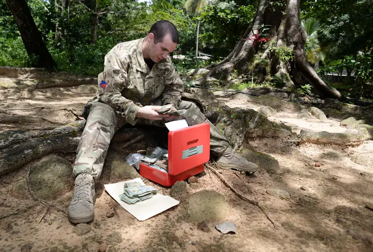 In this photo an Army clerk in camouflage uniform issues local currency to soldiers who have newly arrived abroad in support of an Operation.