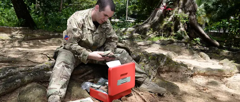 In this photo an Army clerk in camouflage uniform issues local currency to soldiers who have newly arrived abroad in support of an Operation.