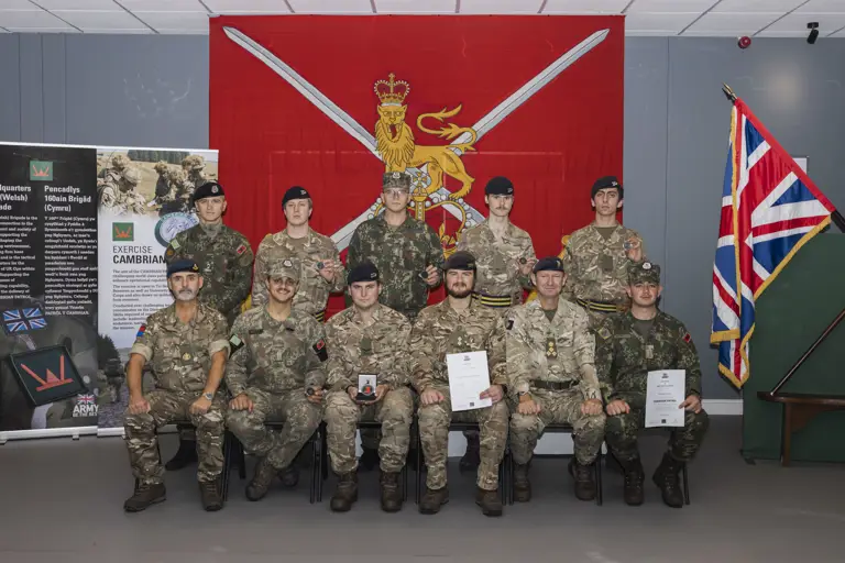 Group of military personnel in uniform posing indoors with a red flag behind them.