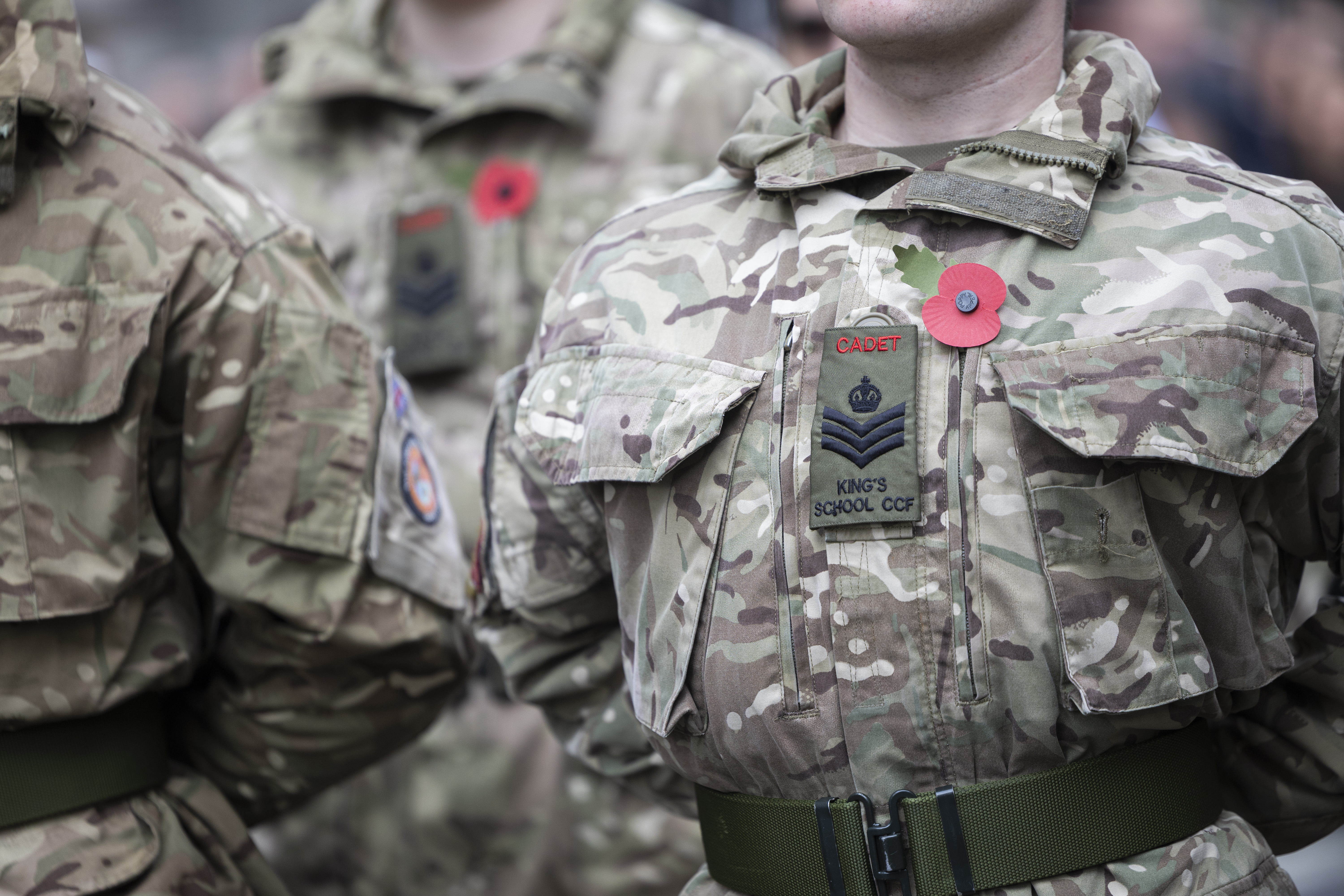 Close-up of Army Cadets in camouflage uniforms wearing red poppy pins for remembrance on their chests.