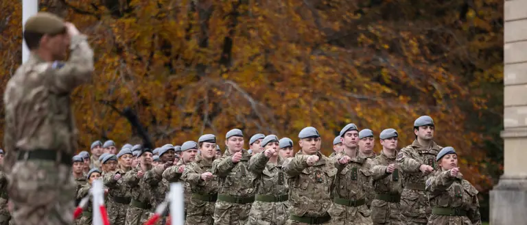 Military personnel in grey berets march in unison.