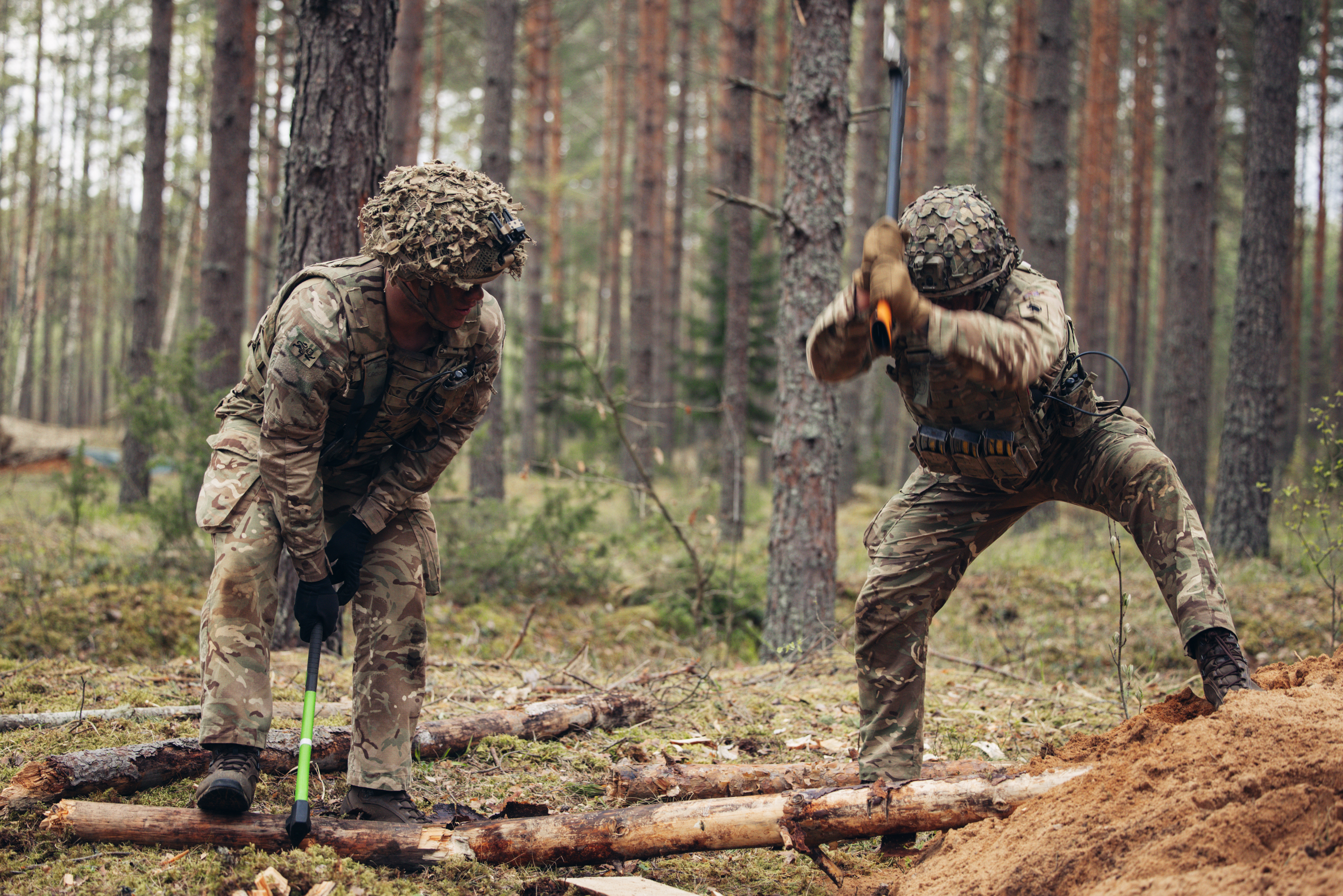 Two soldiers in uniform are pictured chopping wood with an axe.