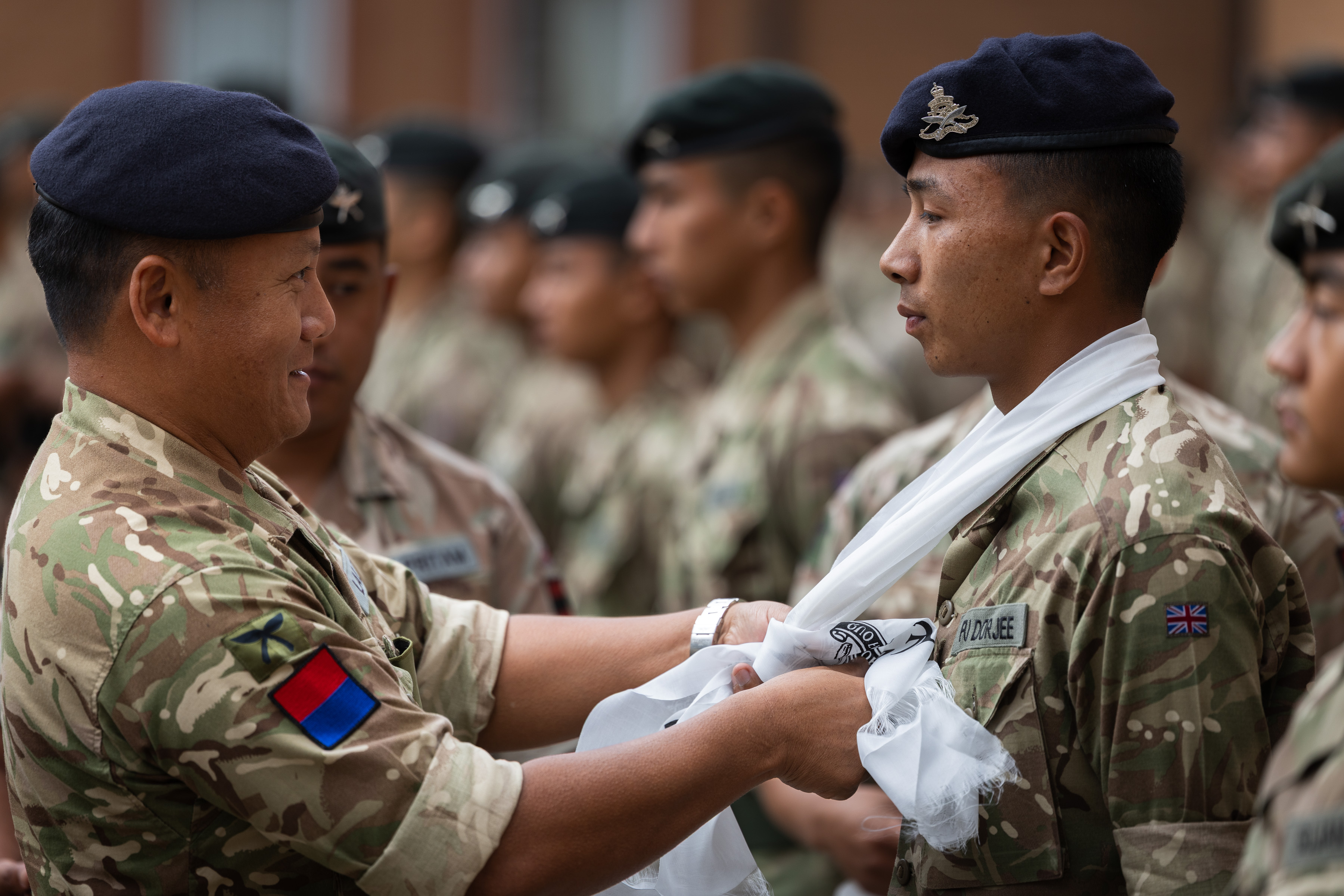A British Army officer is tying a white scarf around the neck of a soldier.