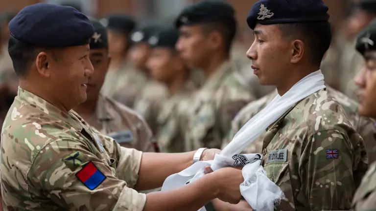 A British Army officer is tying a white scarf around the neck of a soldier.