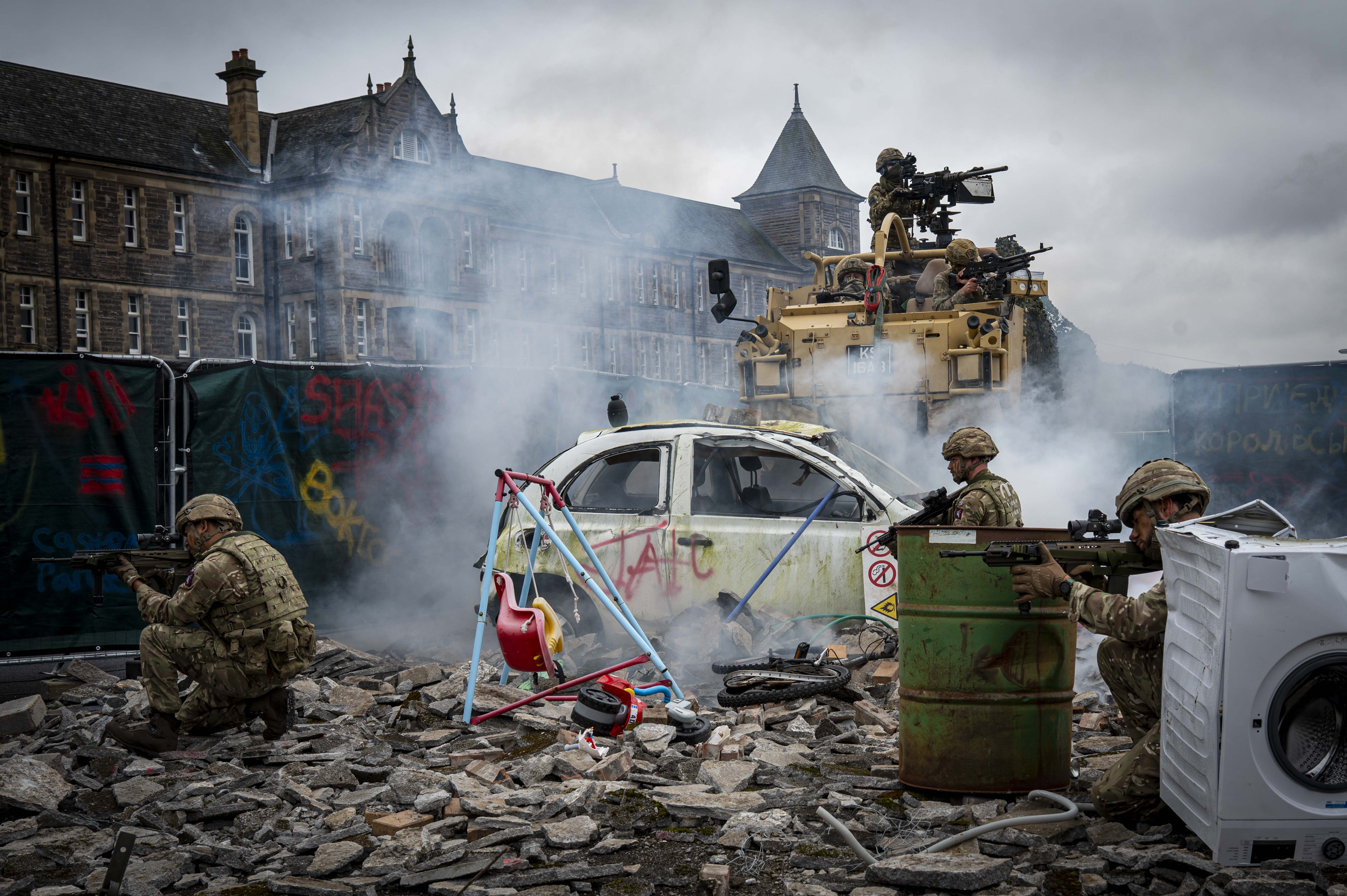 Soldiers shown demonstrate an attack scenario outside with debris including a child's swing, a car and white goods and a jackal with Soldiers in coming through the back.