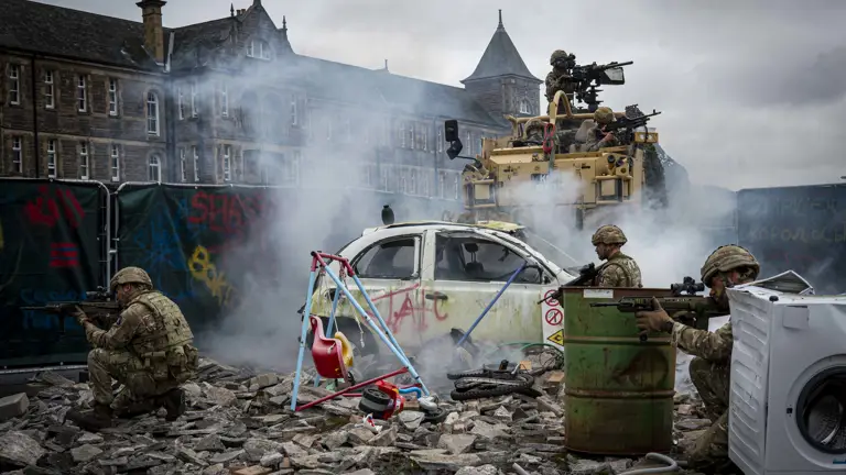 Soldiers shown demonstrate an attack scenario outside with debris including a child's swing, a car and white goods and a jackal with Soldiers in coming through the back.