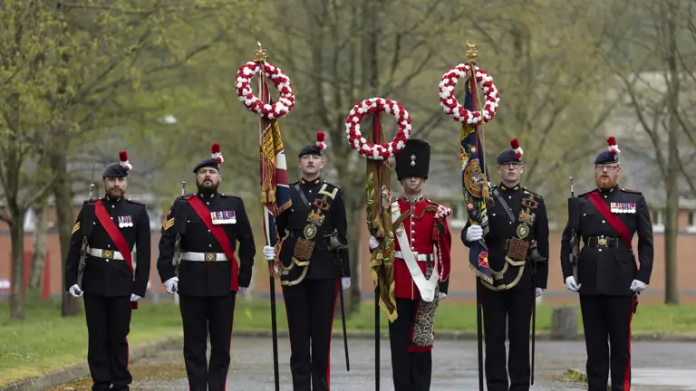 Soldiers in black and red tunics hold banners while stood on parade.