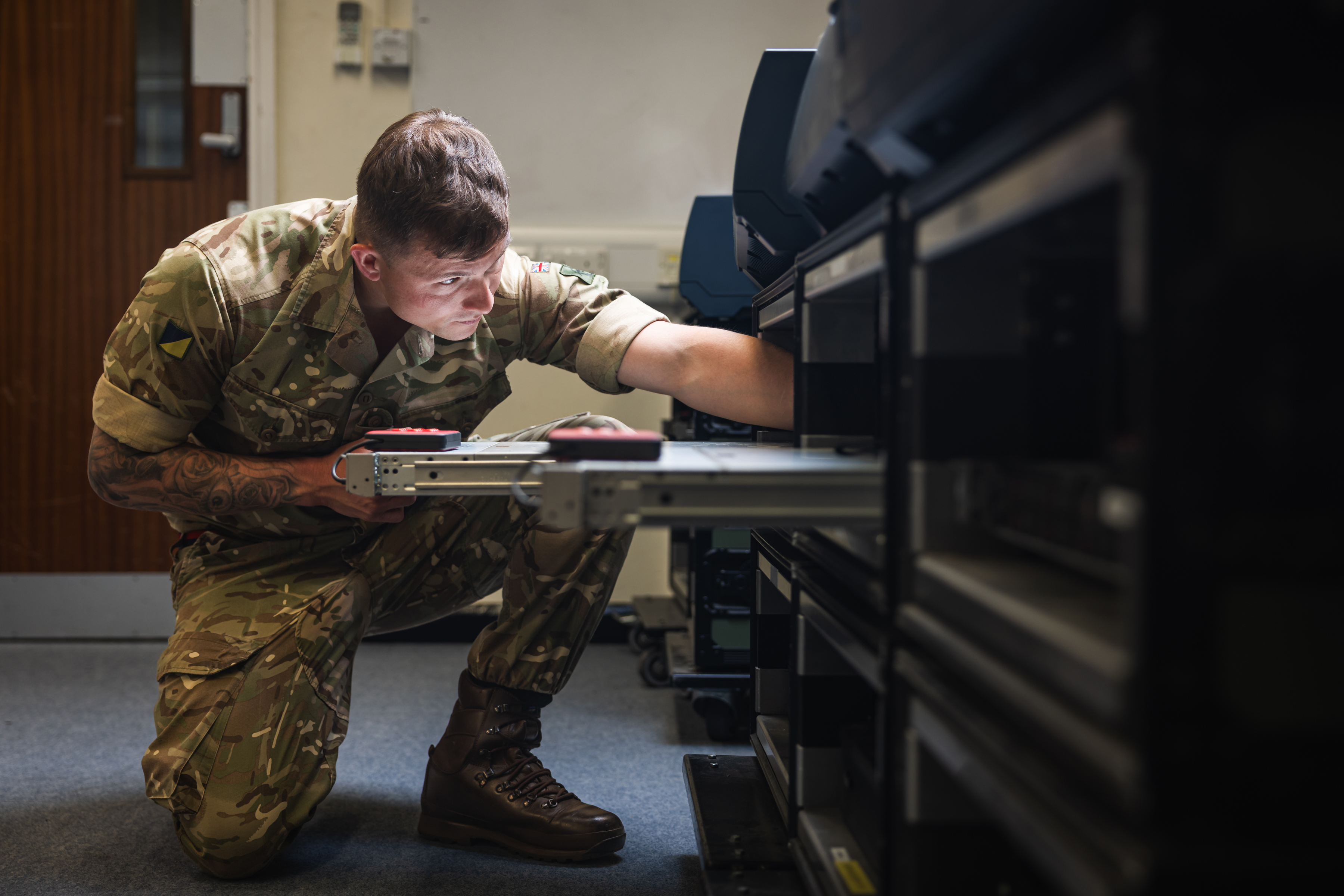 A British Army soldier reaches in to a server rack to adjust cables its cables. 