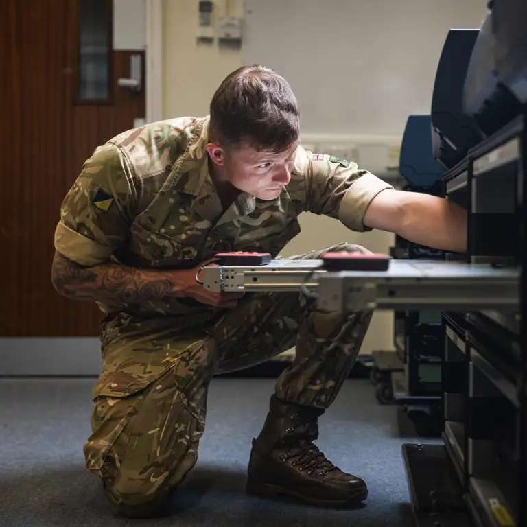A British Army soldier reaches in to a server rack to adjust cables its cables.