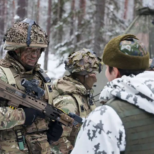 A military vehicle camouflaged with foliage traverses a snowy forest, surrounded by tall pine trees, creating a still, cold, and secretive atmosphere.