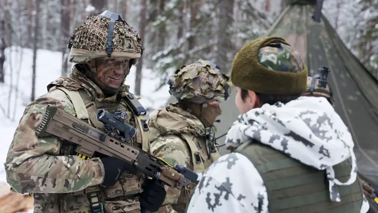 A military vehicle camouflaged with foliage traverses a snowy forest, surrounded by tall pine trees, creating a still, cold, and secretive atmosphere.