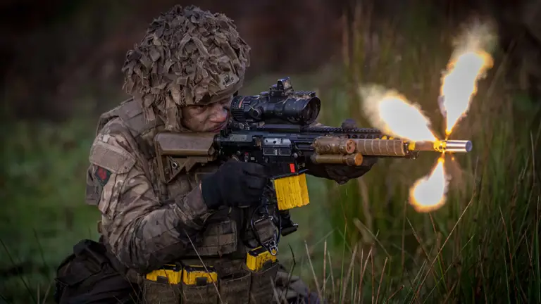 A soldier wearing camouflage uniform fires a rifle.