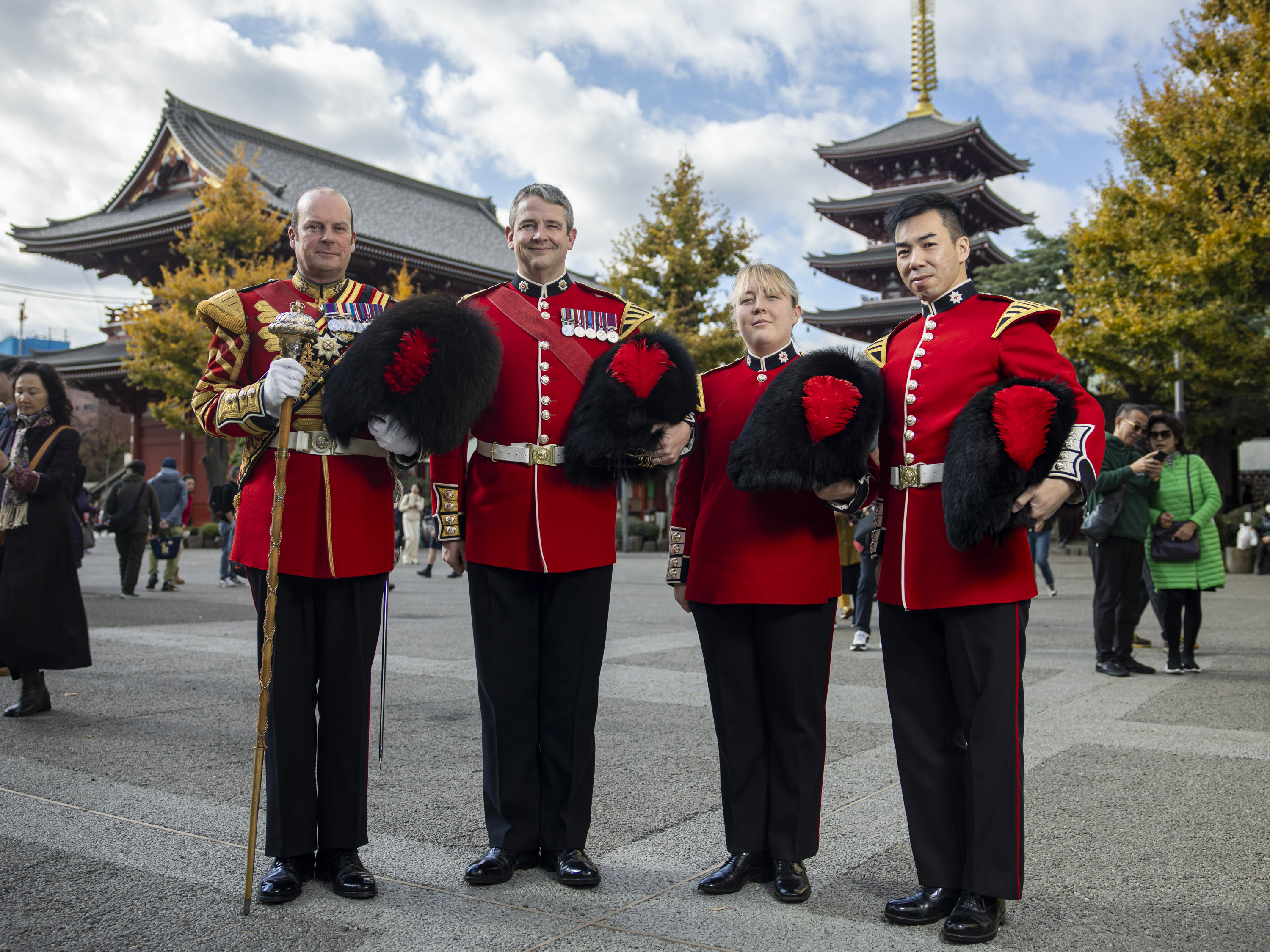 Four soldiers in red tunics hold their bearskin hats outside of an iconic Japanese temple.