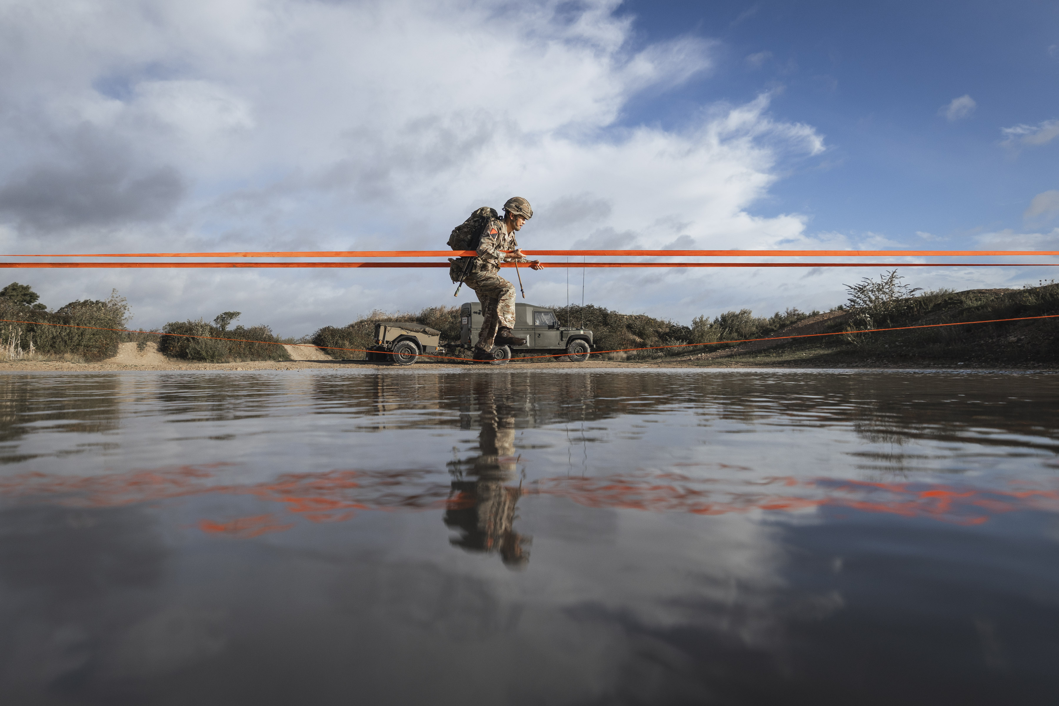 Soldier in full camouflage gear crosses a body of water during a training exercise.