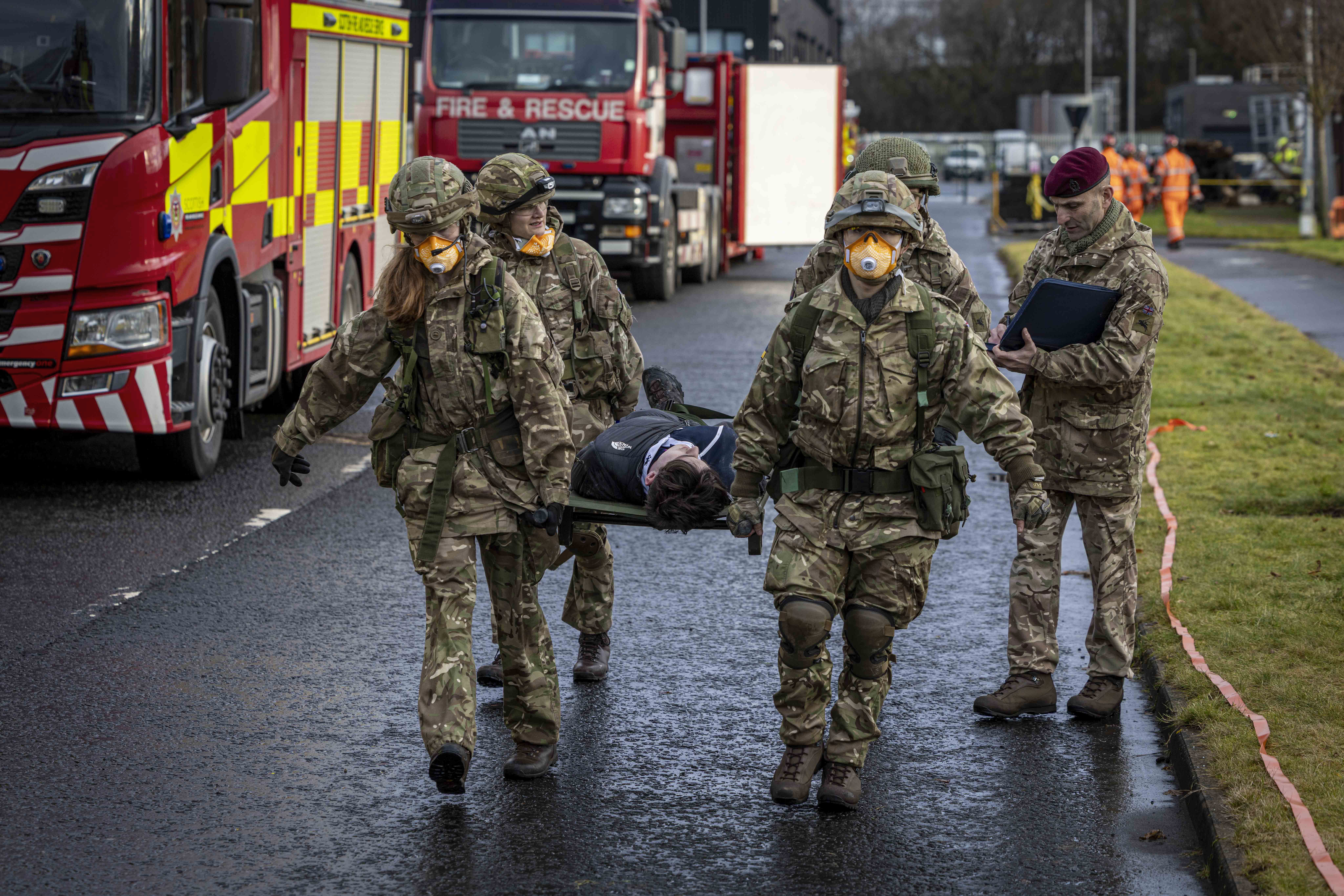 A group of individuals wearing military uniforms and face masks are carrying a person on a stretcher.