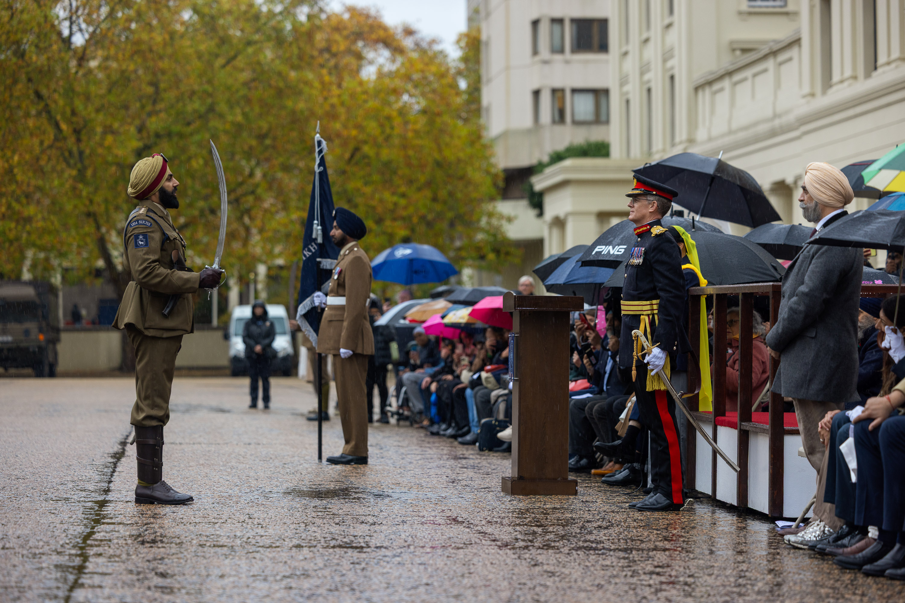 Soldier in traditional uniform holding a sword stands at attention during a formal outdoor ceremony.