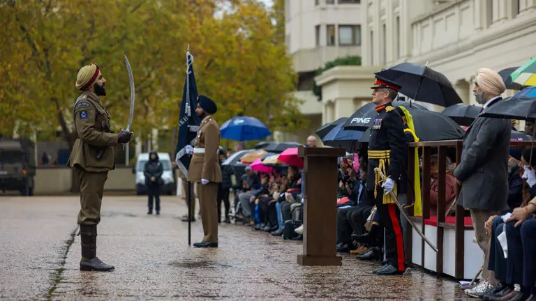 Soldier in traditional uniform holding a sword stands at attention during a formal outdoor ceremony.