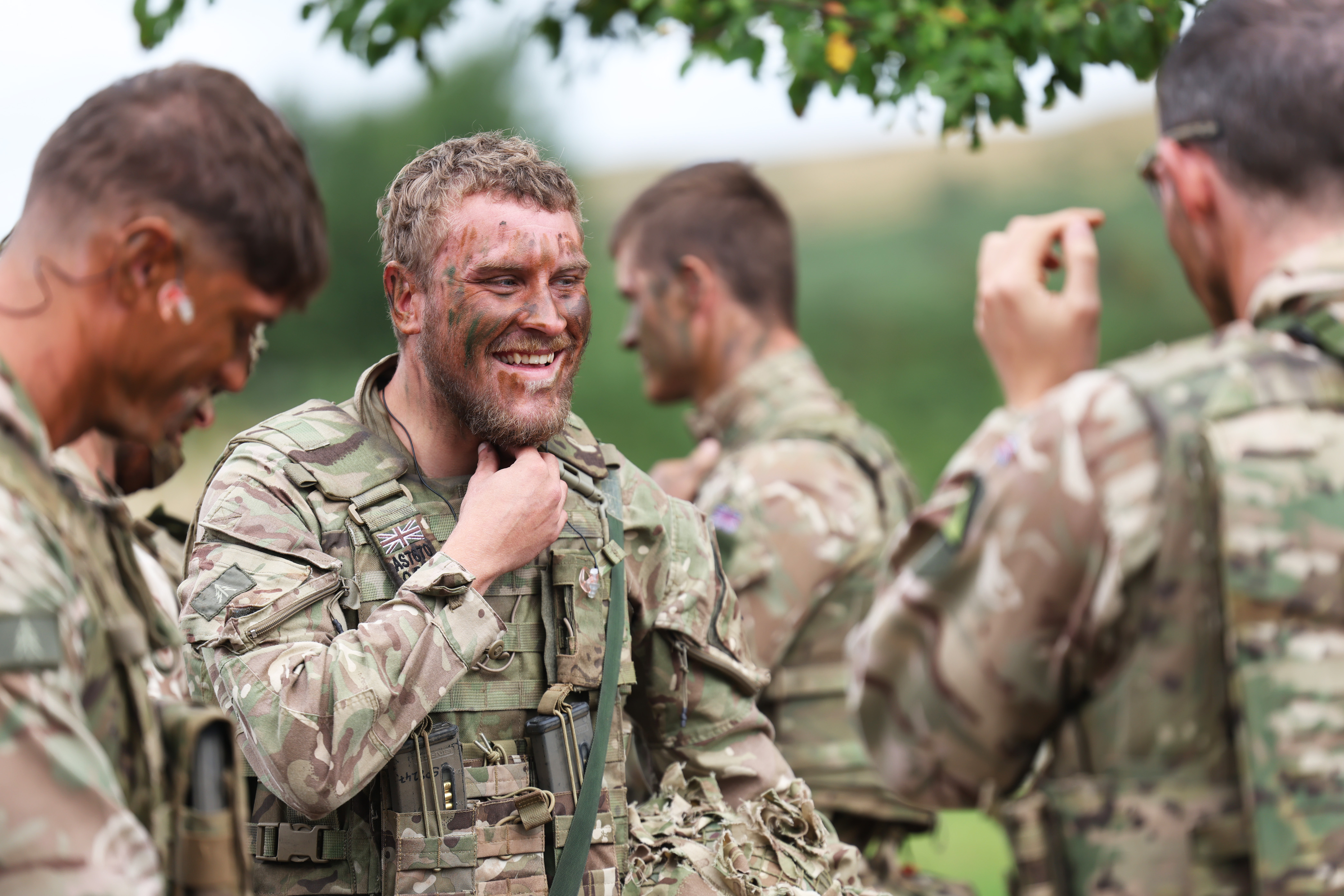Group of soldiers in camouflage uniforms communicating outdoors during a training exercise.