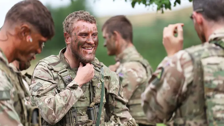 Group of soldiers in camouflage uniforms communicating outdoors during a training exercise.