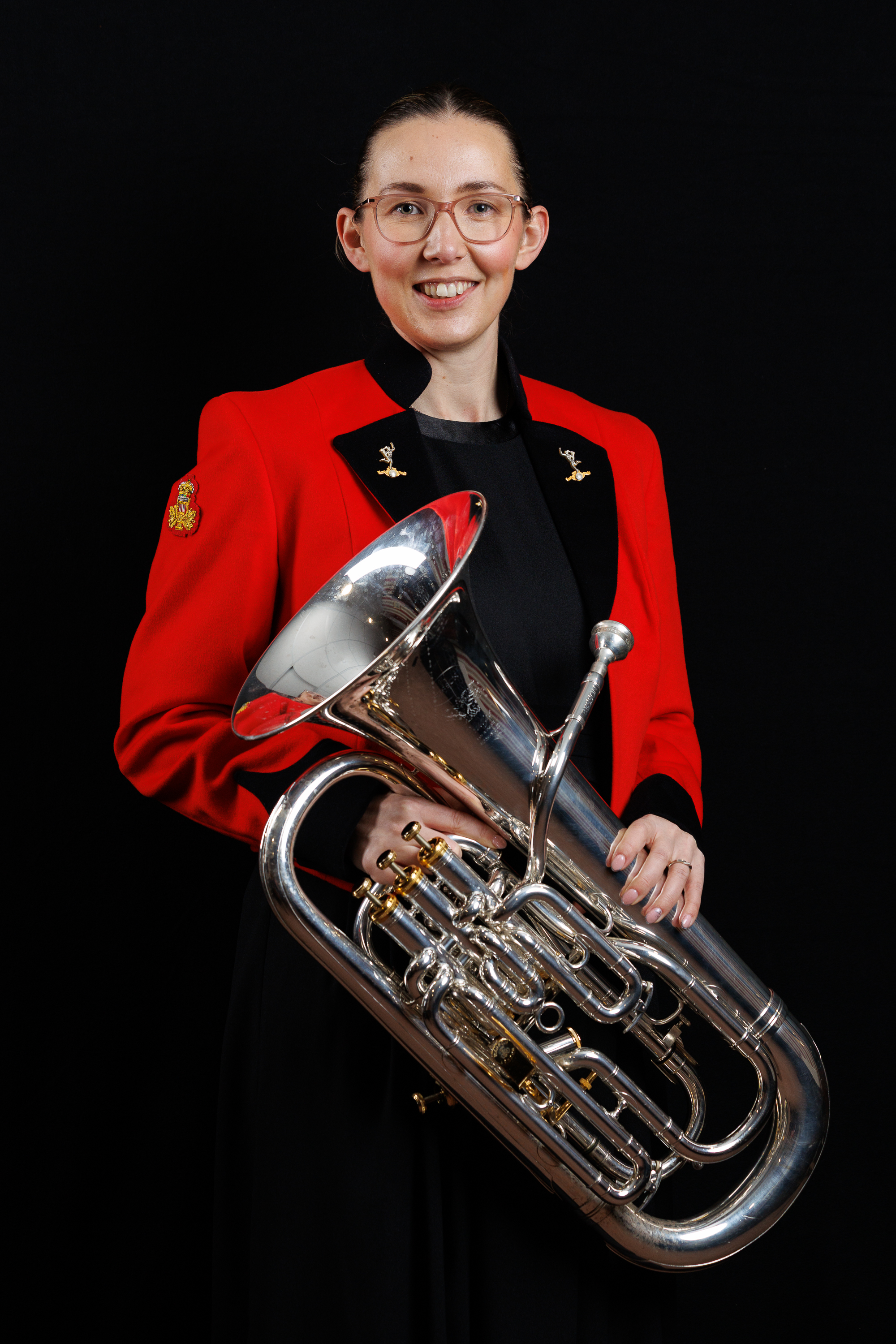Musician in a red jacket holding a shiny silver euphonium against a black background.