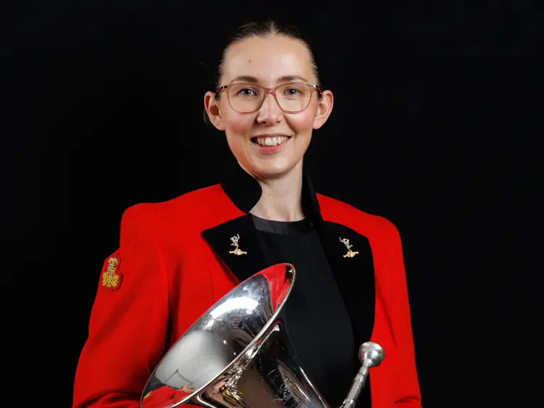 Musician in a red jacket holding a shiny silver euphonium against a black background.