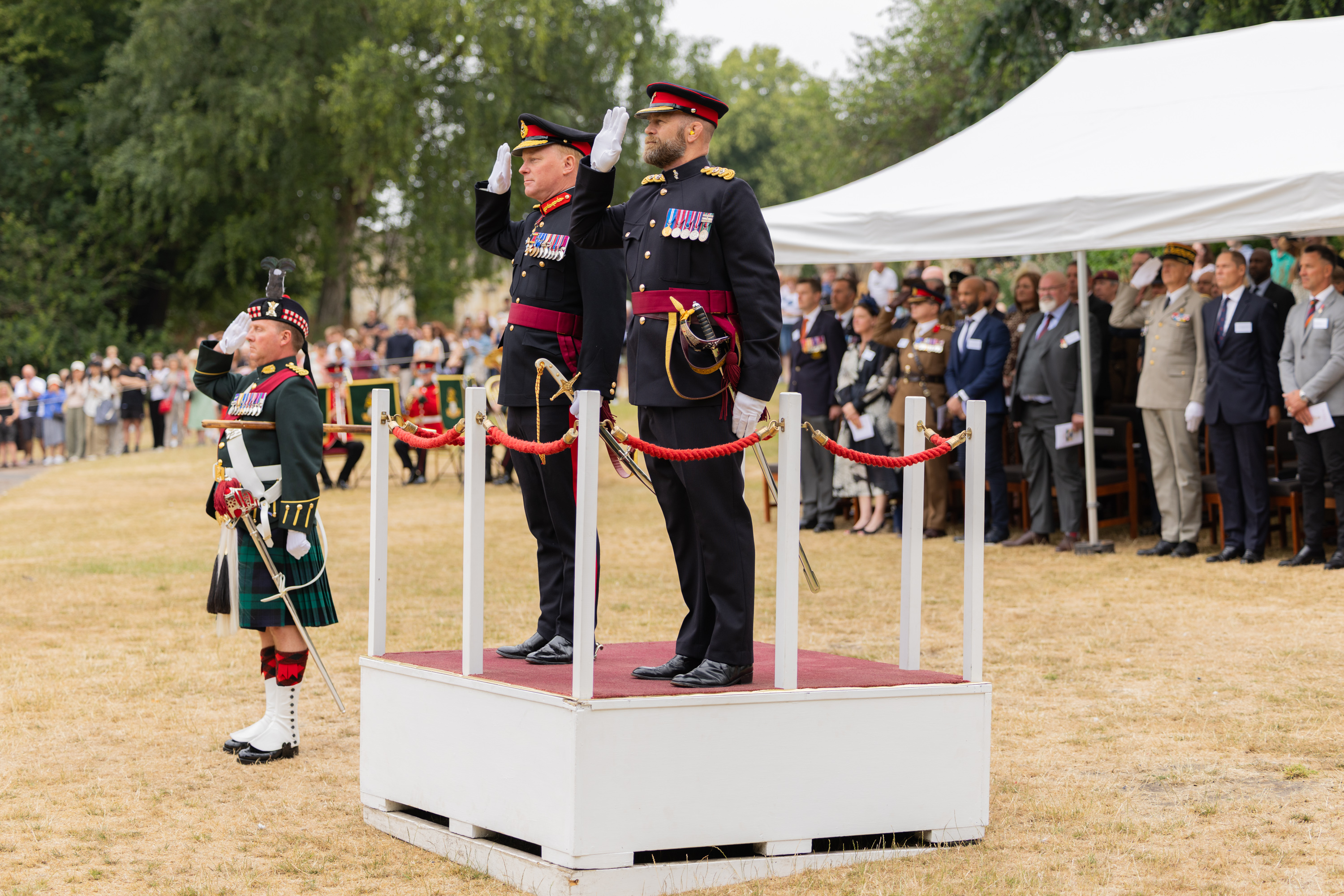 Military officers in formal uniforms stand on a platform, saluting.