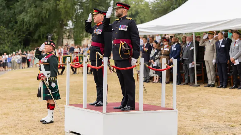 Military officers in formal uniforms stand on a platform, saluting.
