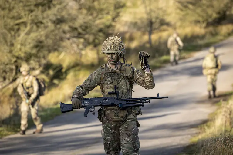 A man in uniform is pictured carrying a weapon and ammunition. 