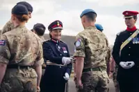 A woman in ceremonial attire smiles as she hands a medal to a soldier in uniform.