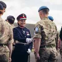 A woman in ceremonial attire smiles as she hands a medal to a soldier in uniform.