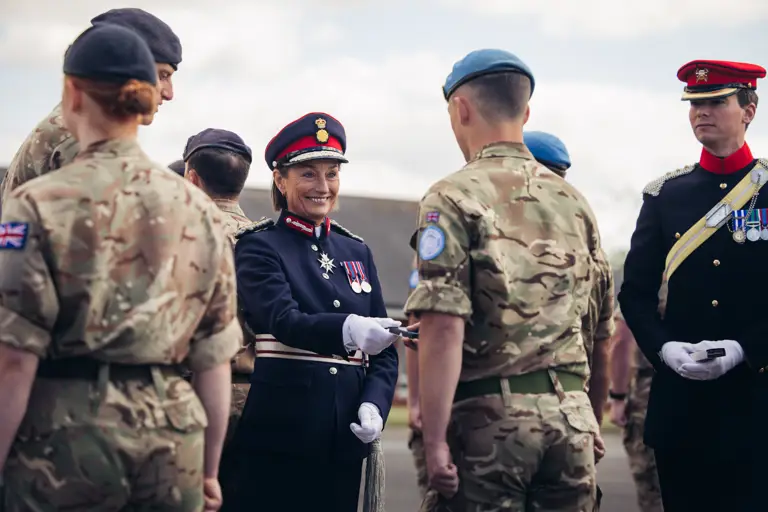 A woman in ceremonial attire smiles as she hands a medal to a soldier in uniform.