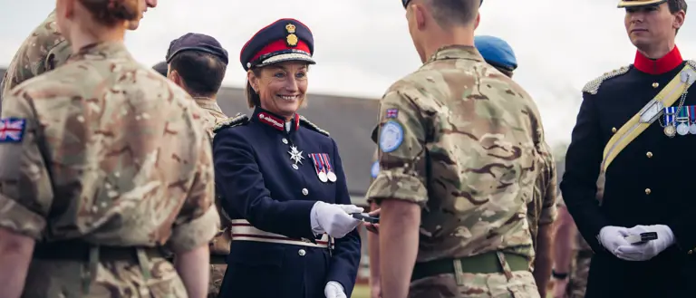 A woman in ceremonial attire smiles as she hands a medal to a soldier in uniform.