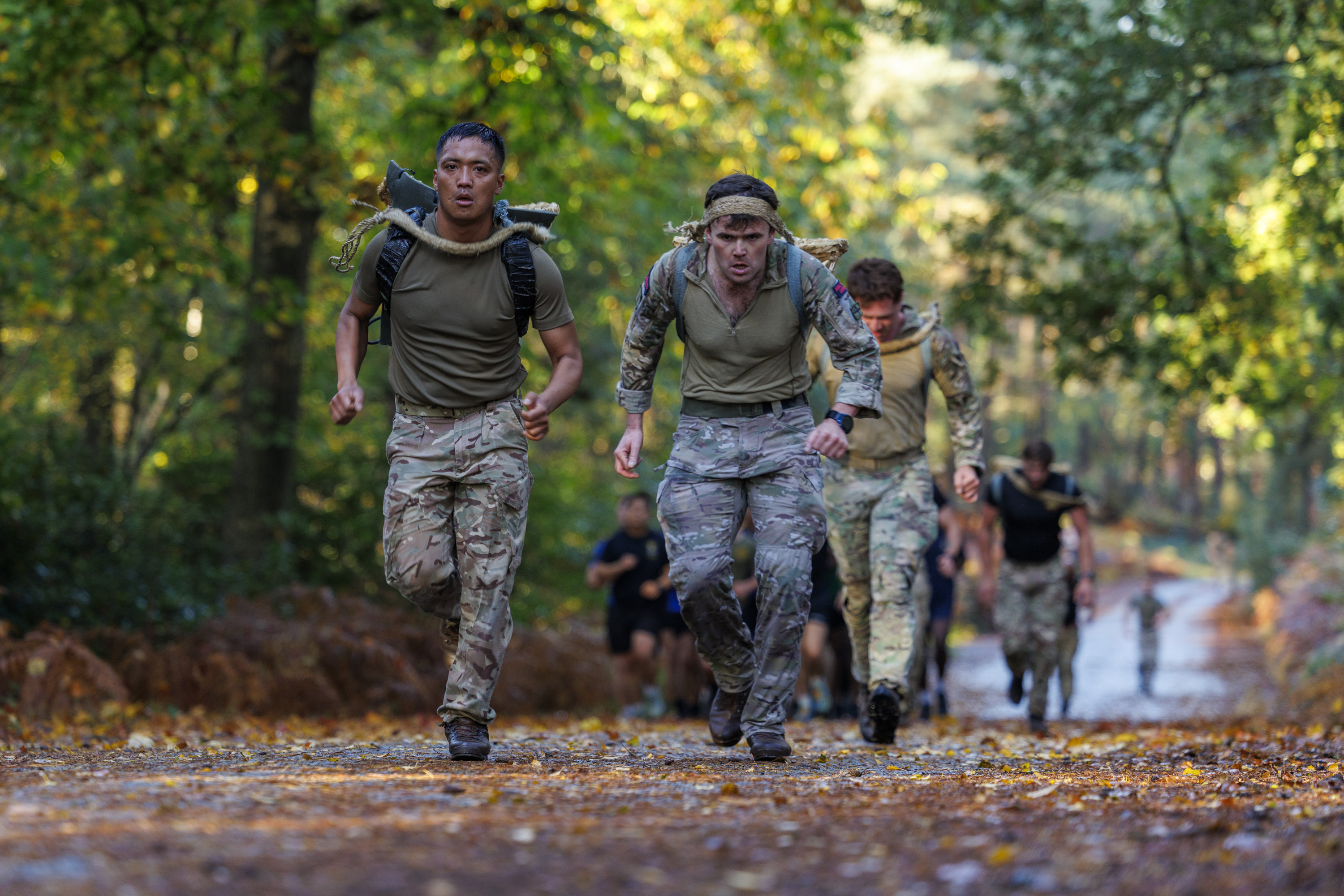 Group of soldiers in camouflage uniforms running on a forest trail during a training exercise.
