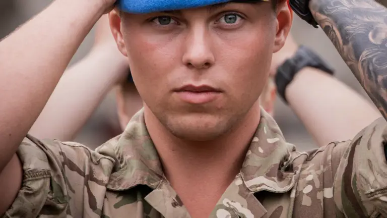 Soldier in camouflage uniform adjusting a blue beret on their head with both hands.
