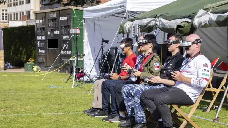 Military personnel not dressed in uniform fly drones whilst seated.