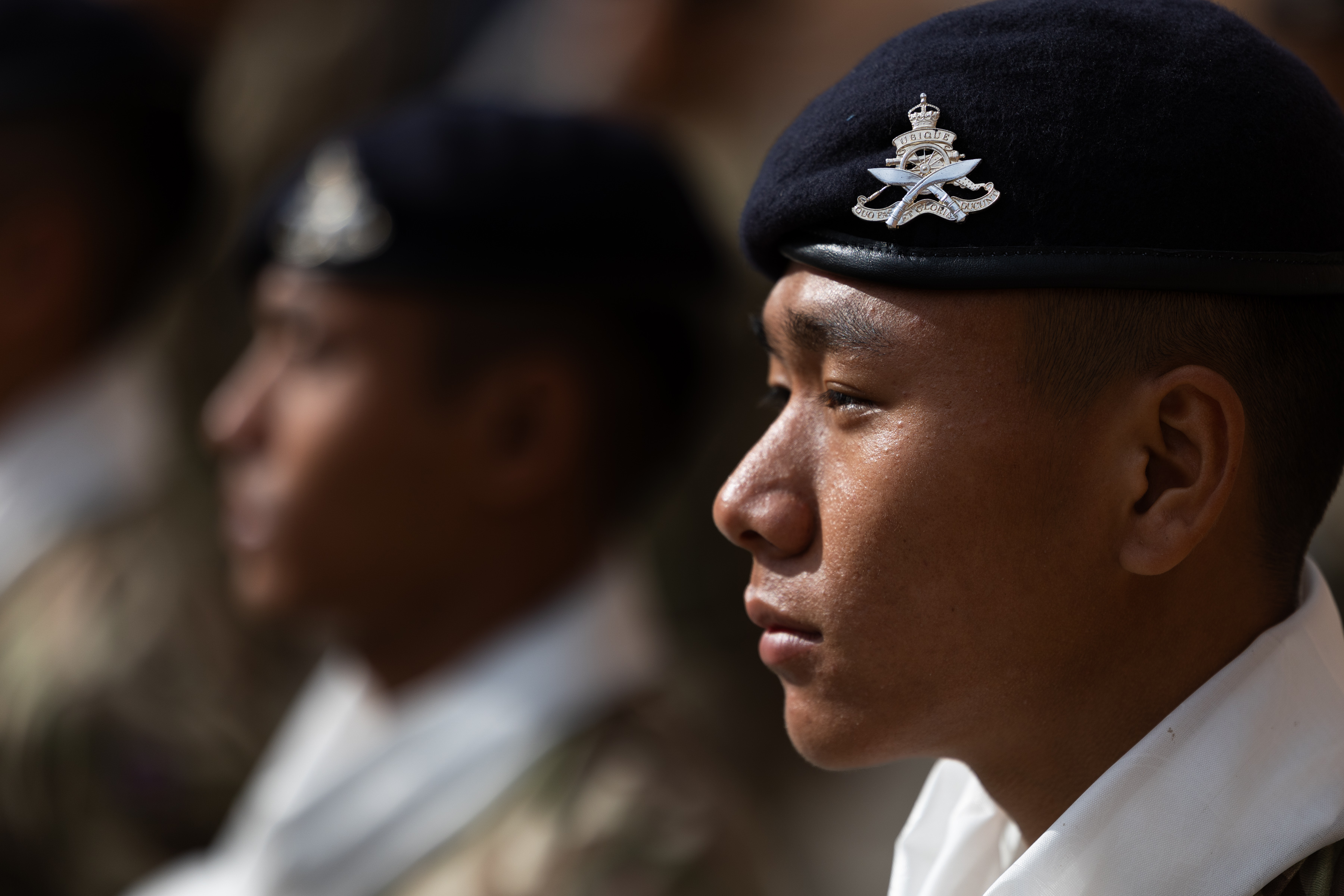 A British Gurkha soldier, facing left to right, has a dark blue beret on his head featuring the cap badge of the King's Gurkha Artillery.