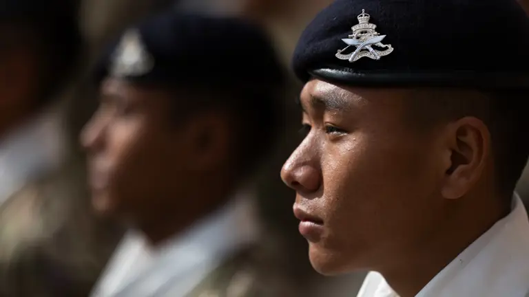 A British Gurkha soldier, facing left to right, has a dark blue beret on his head featuring the cap badge of the King's Gurkha Artillery.