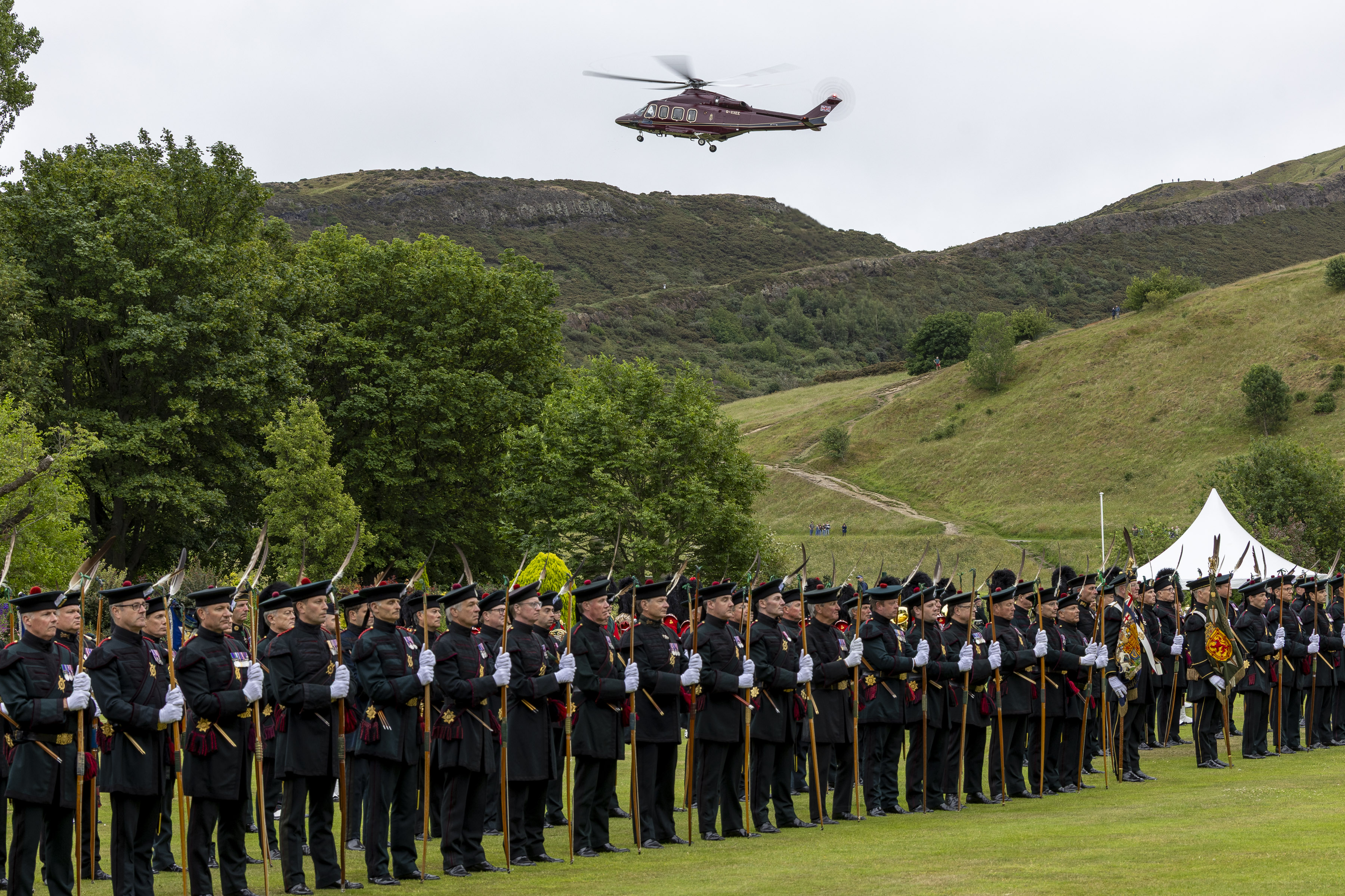 A red helicopter flies over soldiers wearing ceremonial attire.