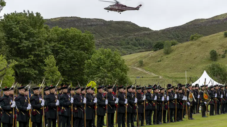 A red helicopter flies over soldiers wearing ceremonial attire.