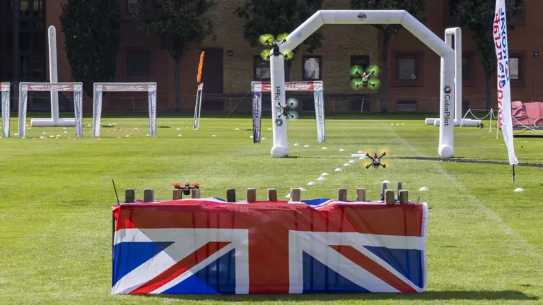 Drones are flown over a table which has a British flag draped over it.
