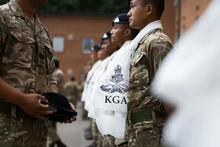 A British Army office is placing a new unit cap badge on a beret for presenting to a soldier.   