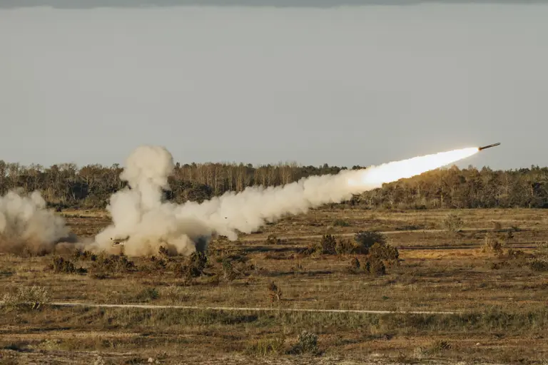Open and empty tree filled landscape shows a reduced range practise rocket having been fired with a plume of smoke behind it.
