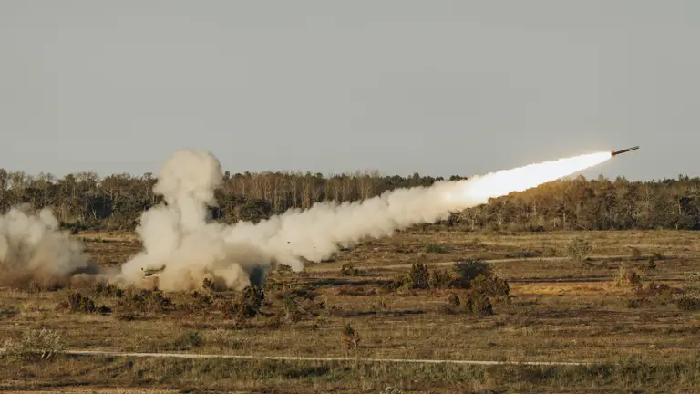 Open and empty tree filled landscape shows a reduced range practise rocket having been fired with a plume of smoke behind it.