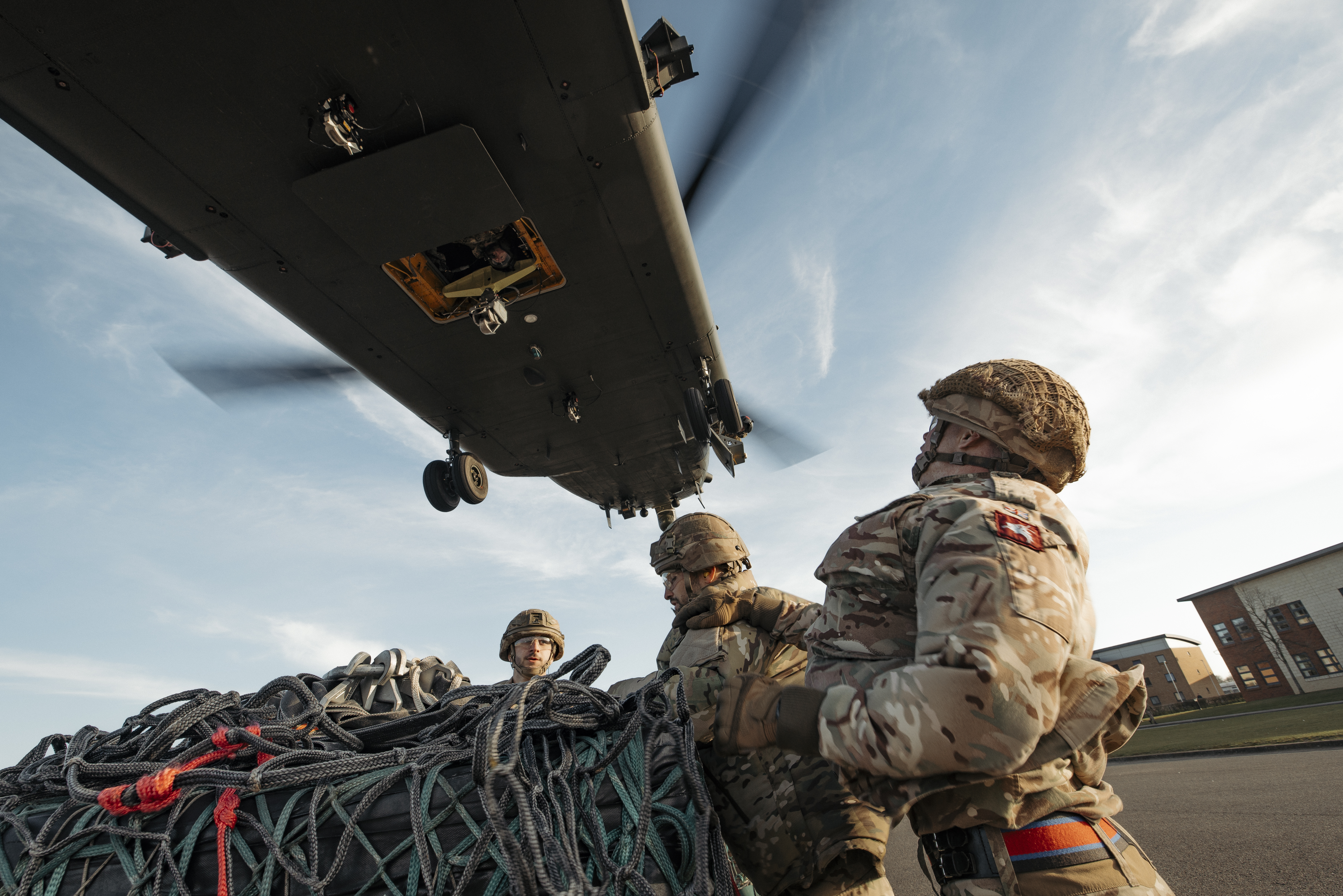 Soldiers wearing their camouflage uniform and helmets stand waiting with a load as a chinook coming into be loaded.